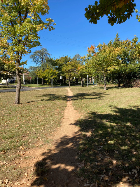 A desire path diagonally across a green area in Canberra, Australia. From the depth of the path, it’s well-worn, frequently used.