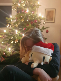 An image of Erik Uden and Oskar the Mastodon plushie snuggling cutely in front of a Christmas tree. In the background is an image of Friedrich Uden, the oldest surviving visual record of a 19th century ancestor of Erik Uden.