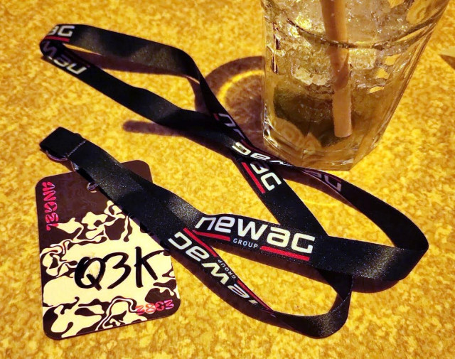 A 38C3 angel badge for 'Q3K' equipped with a Newag Group lanyard. On a table, next to a half-finished tschunk.