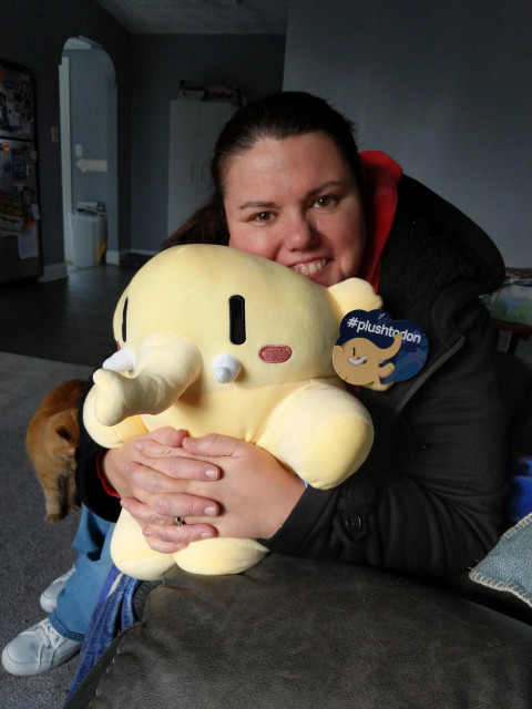 Black haired woman holding a yellow mastodon stuffed animal.