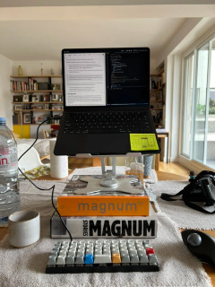 Planck EZ keyboard on a dining table connected to a laptop raised on a pile of books, travel mode