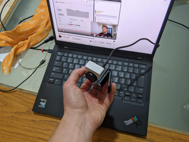 Holding a webcamera in my left hand in from of my thinkpad laptop.