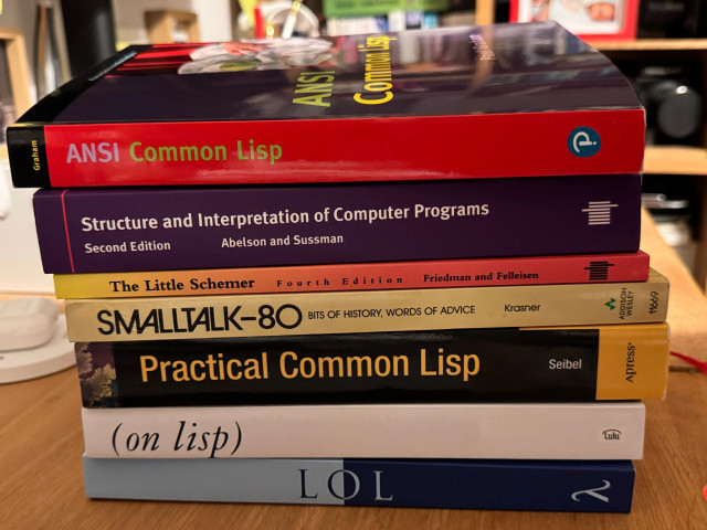 A stack of books related to programming, on a desk. From top to bottom:
- ANSI Common Lisp
- SICP
- The Little Schemer
- Smalltalk-80: bits of history, words of advice
- Practical Common Lisp
- On Lisp
- Let Over Lambda