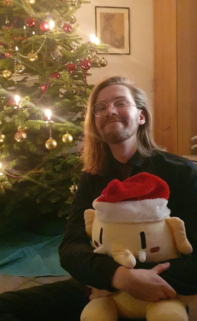 An image of Erik Uden and Oskar the Mastodon plushie hugging in front of a Christmas tree. In the background is an image of Friedrich Uden, the oldest surviving visual record of a 19th century ancestor of Erik Uden.