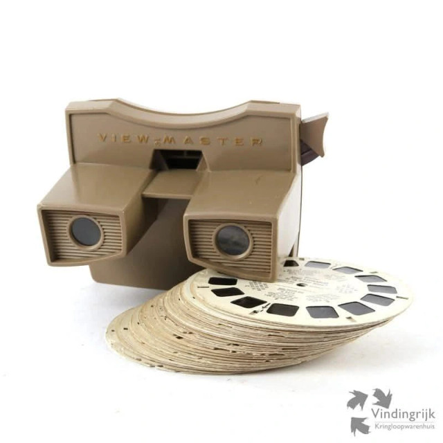 A light brown viewmaster with a pack of viewmaster photo cards next to it.
Thin cardboard disks containing Stereoscopic 3-D pairs of small transparent color photographs on film.
The View-Master system was introduced in 1939.