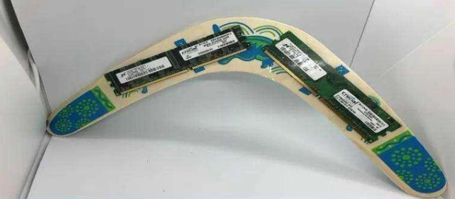 The image shows a boomerang with two RAM sticks attached to it. The boomerang is made of wood and has a blue and green design. 