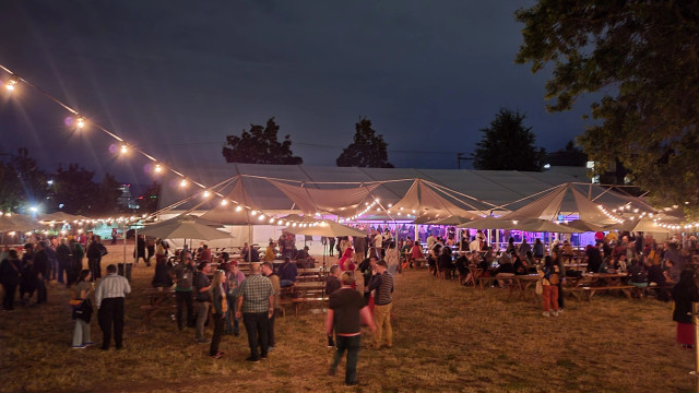 A large tent and many people under strings of lights at night 