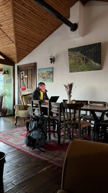 A cozy house. A man in the green fleece and sporty dark jacket sitting at the wooden table and staring into laptop's screen.